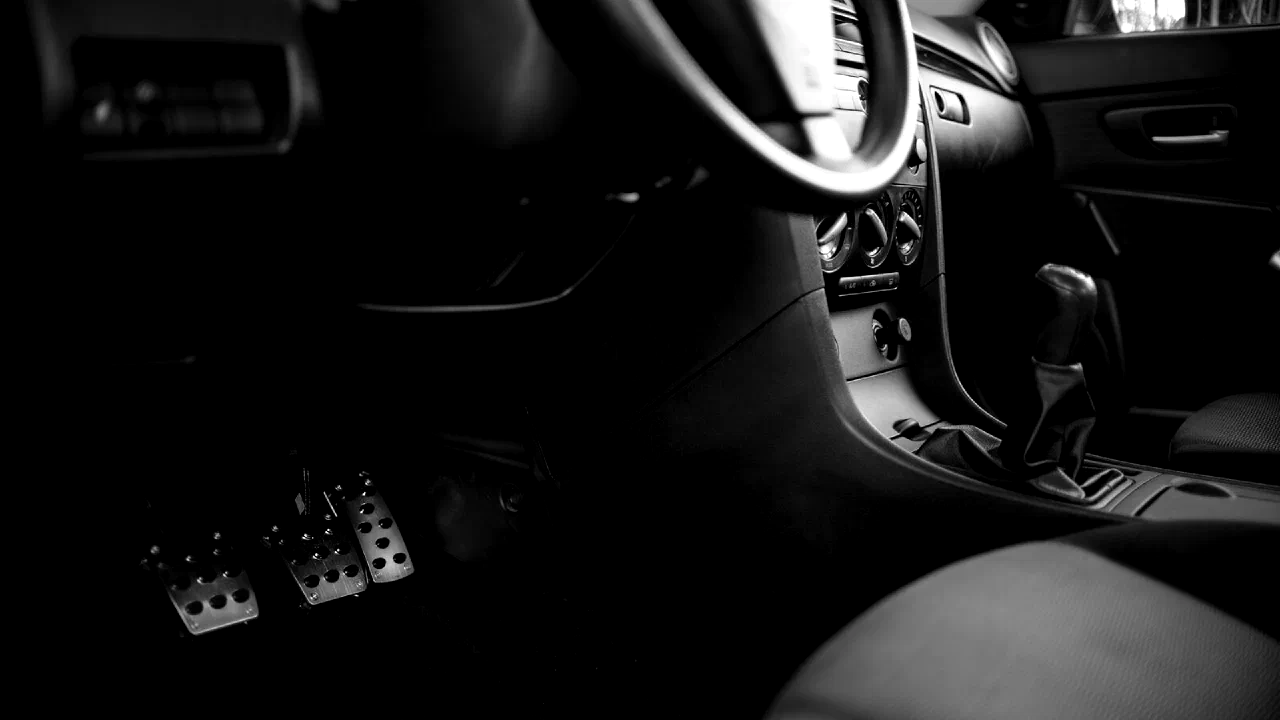 The pedals and footwell of a car interior, photographed in black and white