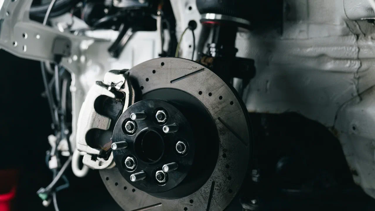 A close-up of a car's front brake disc and caliper behind an alloy wheel