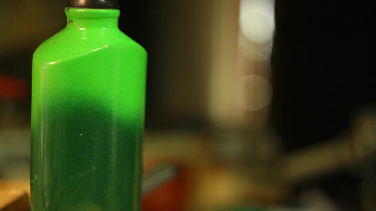 A green bottle holding a dark liquid
