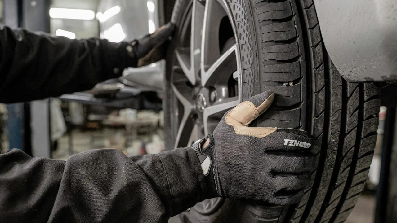 A person in work gloves removing a wheel from a car in a garage